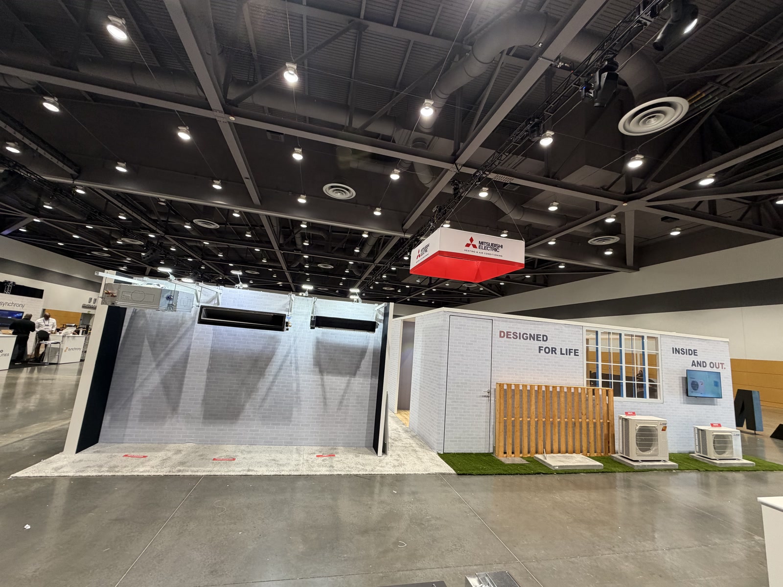 Wide view of Mitsubishi Electric HVAC booth with branded hanging sign, product zones, and exterior display elements.