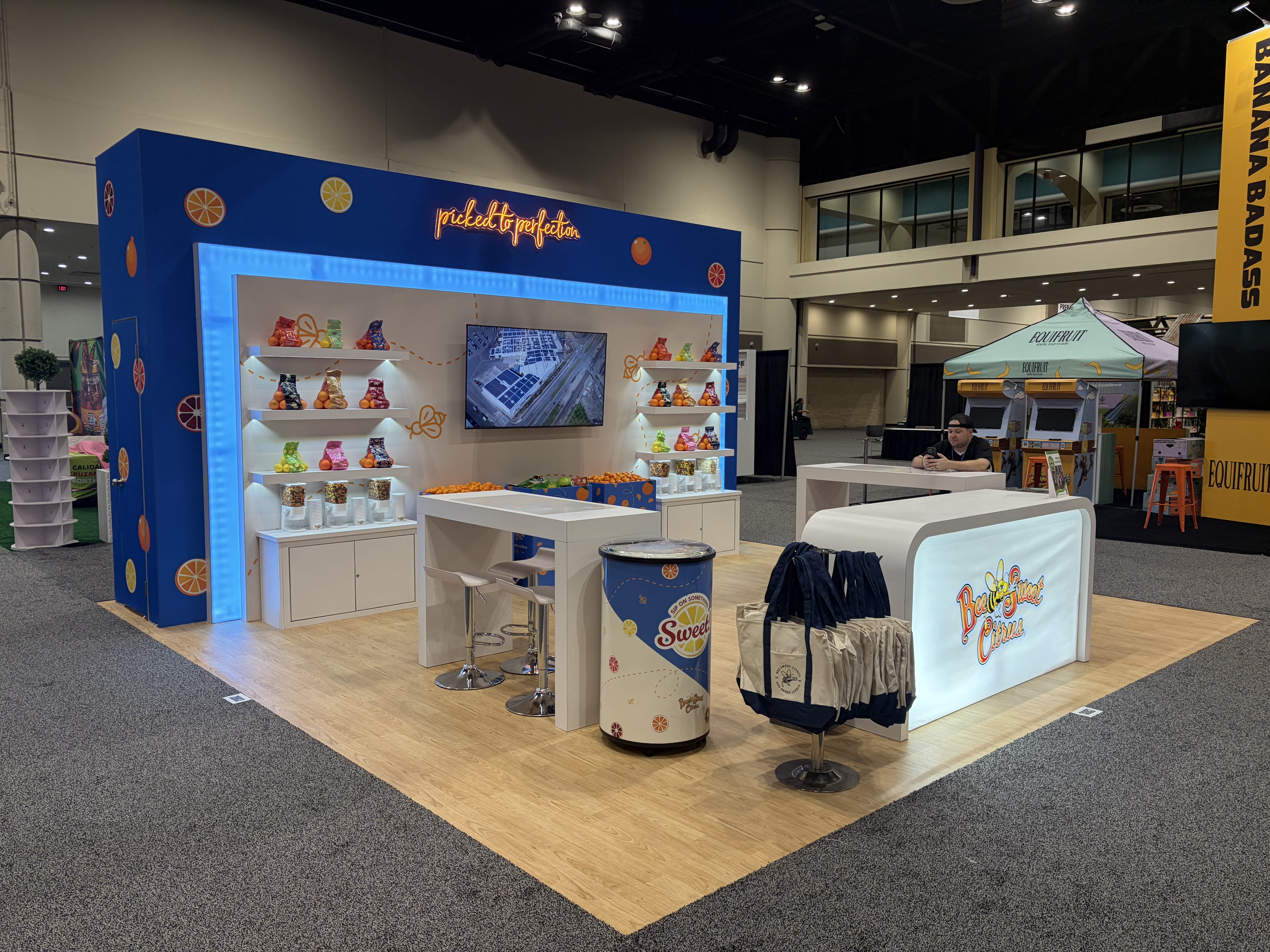 Bee Sweet Citrus exhibit with a blue illuminated display wall, citrus packages on white shelves, meeting counters and a lighted reception counter