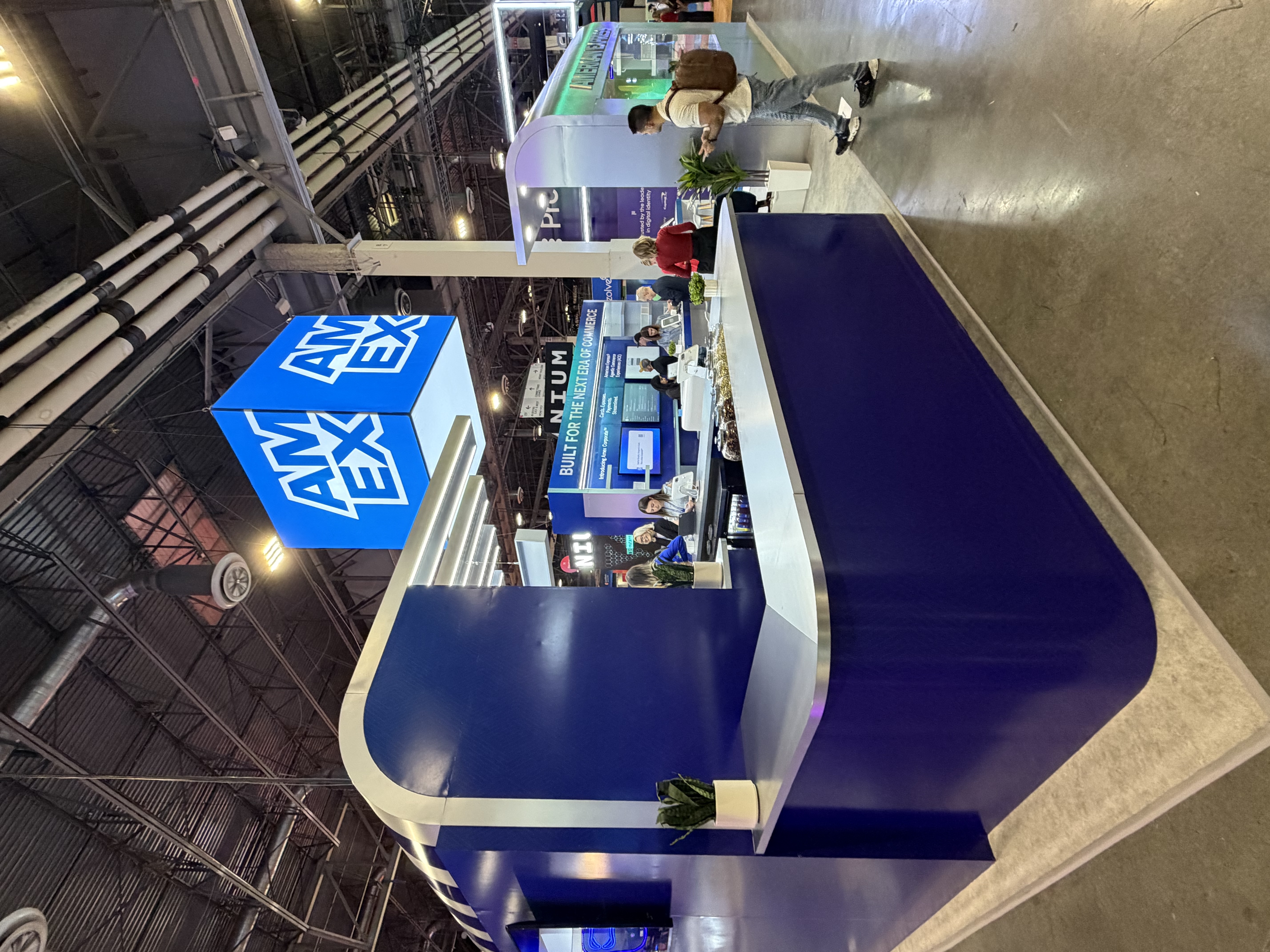 American Express exhibit with blue counters, illuminated overhead elements and suspended branding.