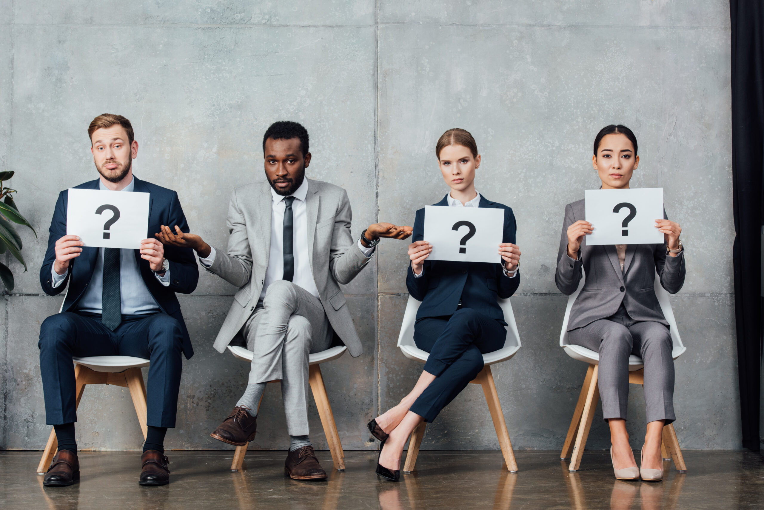 multiethnic businesspeople holding cards with question marks in waiting hall